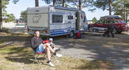 man sitter i campingstol framför Polar husvagn på campingplats
