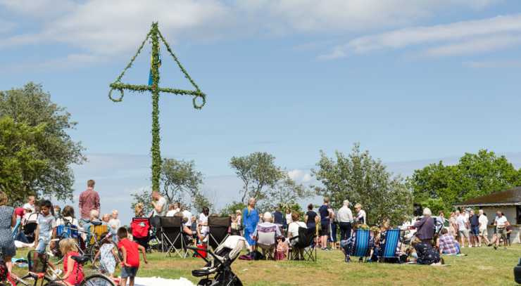 Midsommarstång mot blå himmel, människor runtomkring