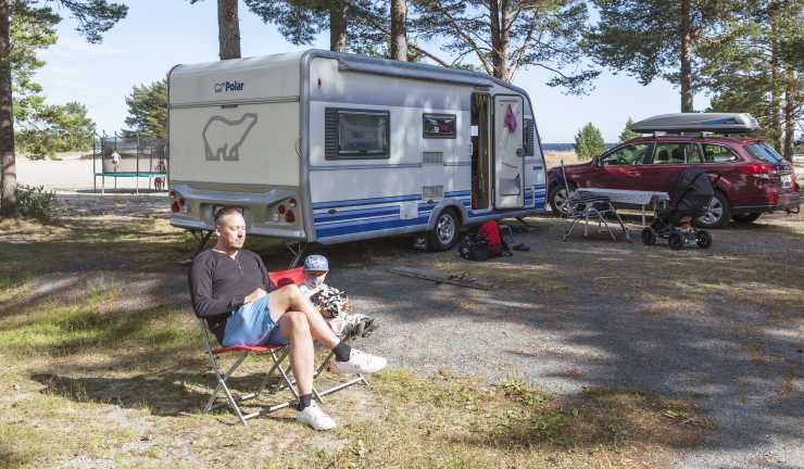 man sitter i campingstol framför Polar husvagn på campingplats