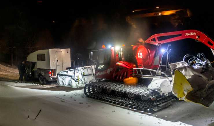 Camper har kört fast i snöig backe får hjälp av pistmaskin.