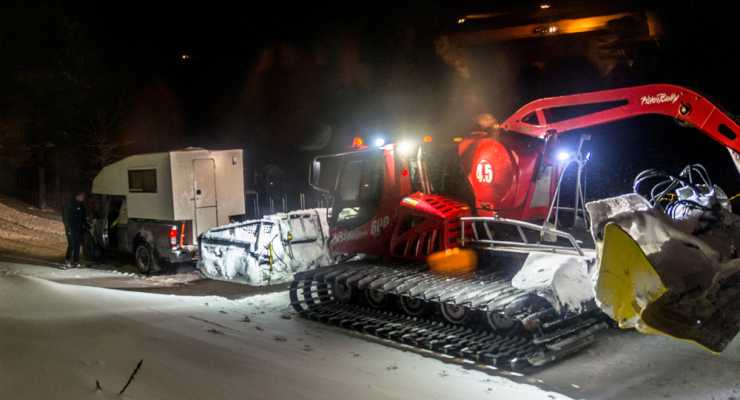 Camper har kört fast i snöig backe får hjälp av pistmaskin.